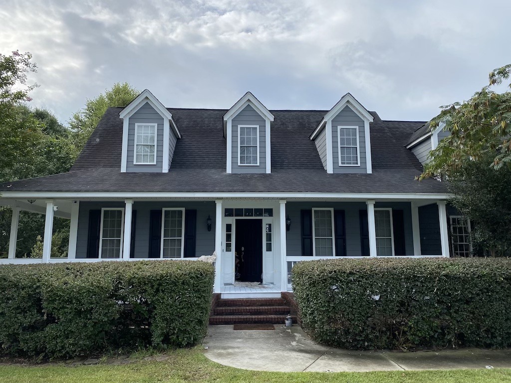 Exterior view of a well-maintained traditional house with a large porch, dark siding, and white trim, show casing a completed home renovation