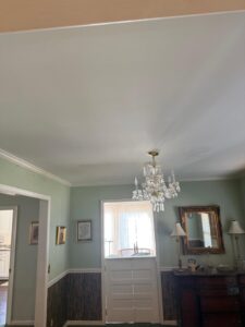 Finished ceiling repaint in Columbia, SC, showing a crisp white flat finish with perfectly straight cut-in lines along the blue walls and a clean, reinstalled chandelier.